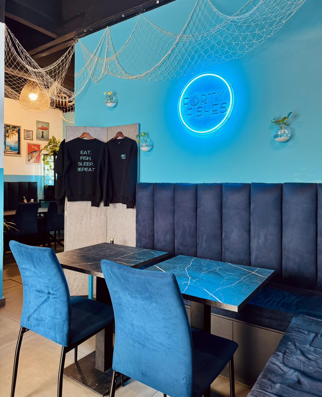 Blue velvet seating, neon logo and Eat Fish Sleep Repeat merch